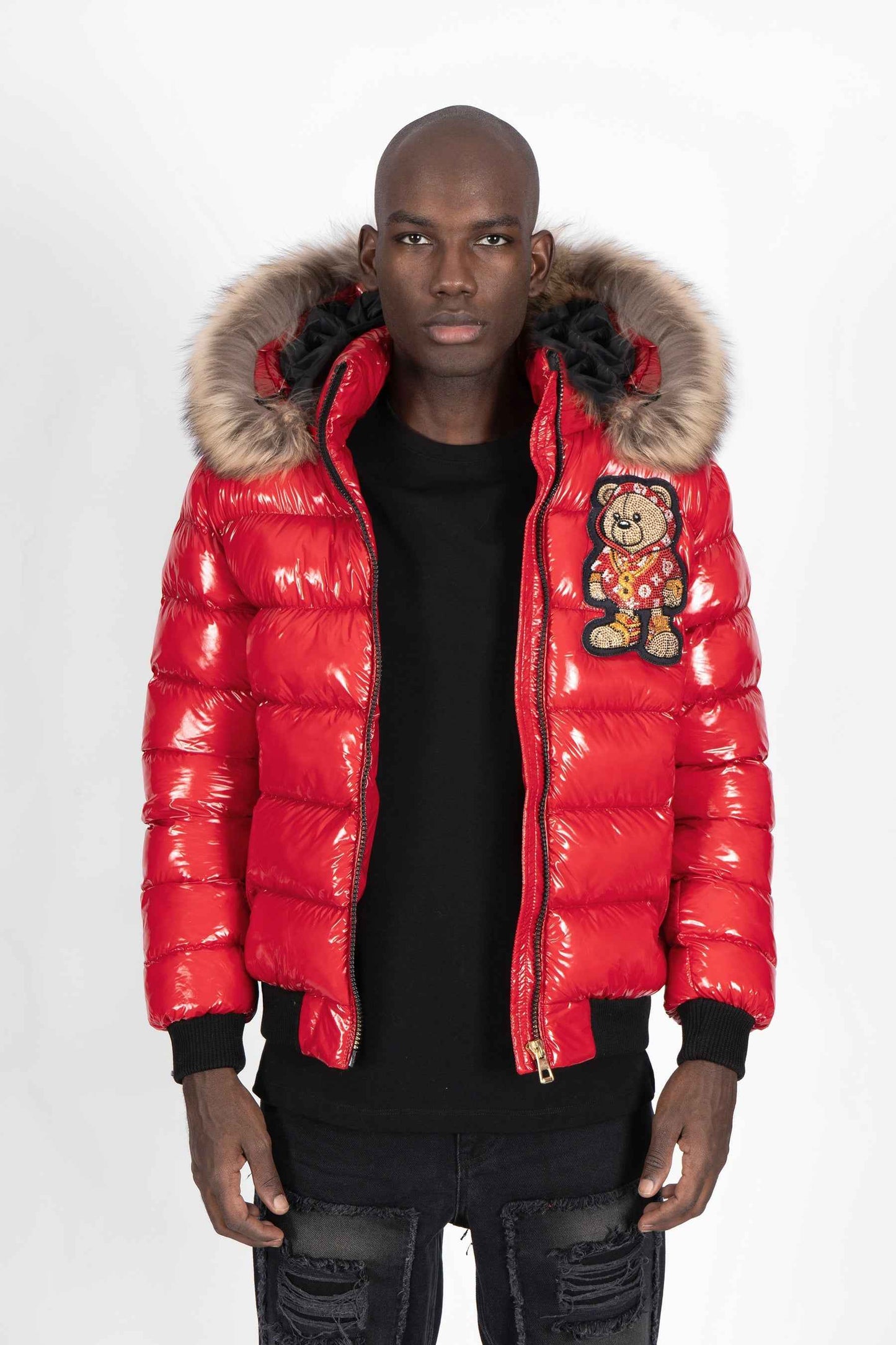 Vista delantera de un modelo luciendo una chaqueta plumífero de color rojo brillante original con una gran capucha de pelo y un parche gigante de un osito gánster con sudadera monograma en la espalda.