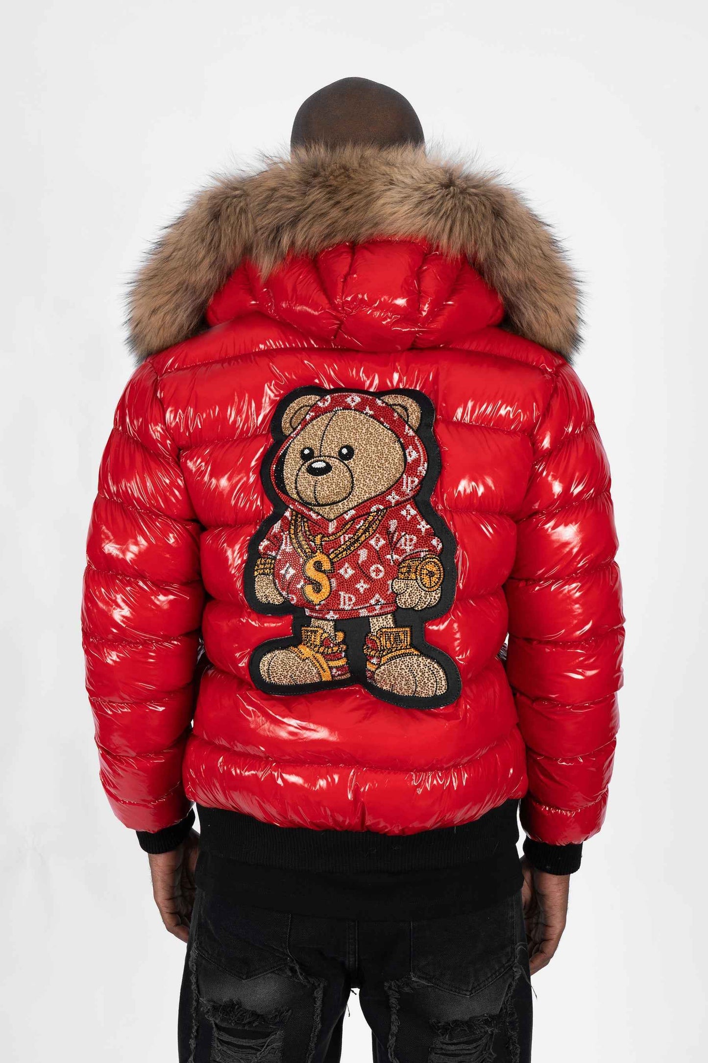 Vista trasera de un modelo luciendo una chaqueta plumífero de color rojo brillante original con una gran capucha de pelo y un parche gigante de un osito gánster con sudadera monograma en la espalda.