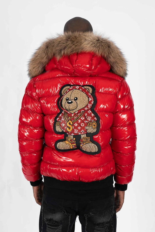 Vista trasera de un modelo luciendo una chaqueta plumífero de color rojo brillante original con una gran capucha de pelo y un parche gigante de un osito gánster con sudadera monograma en la espalda.